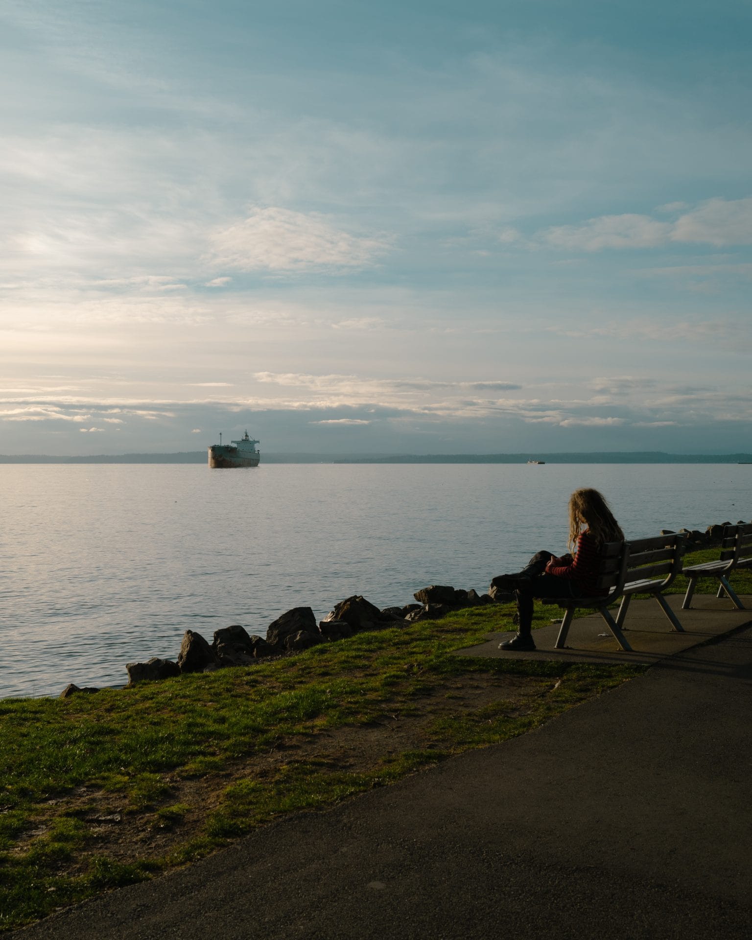 A person sitting on a bench at the Seattle Water Front admiring the Puget Sound